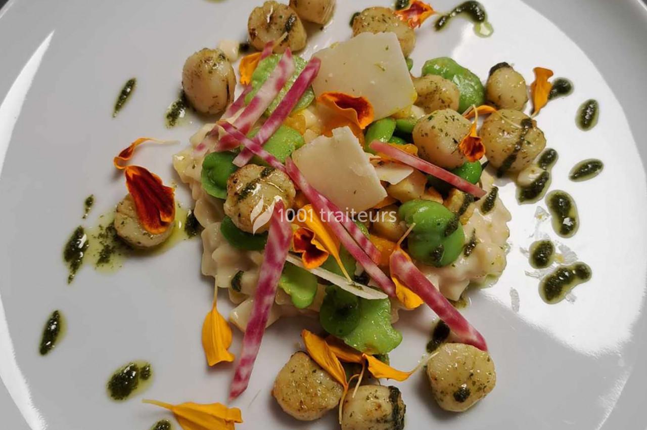 Assiette de gnocchis avec légumes colorés, copeaux de fromage, fleurs comestibles et sauce verte.