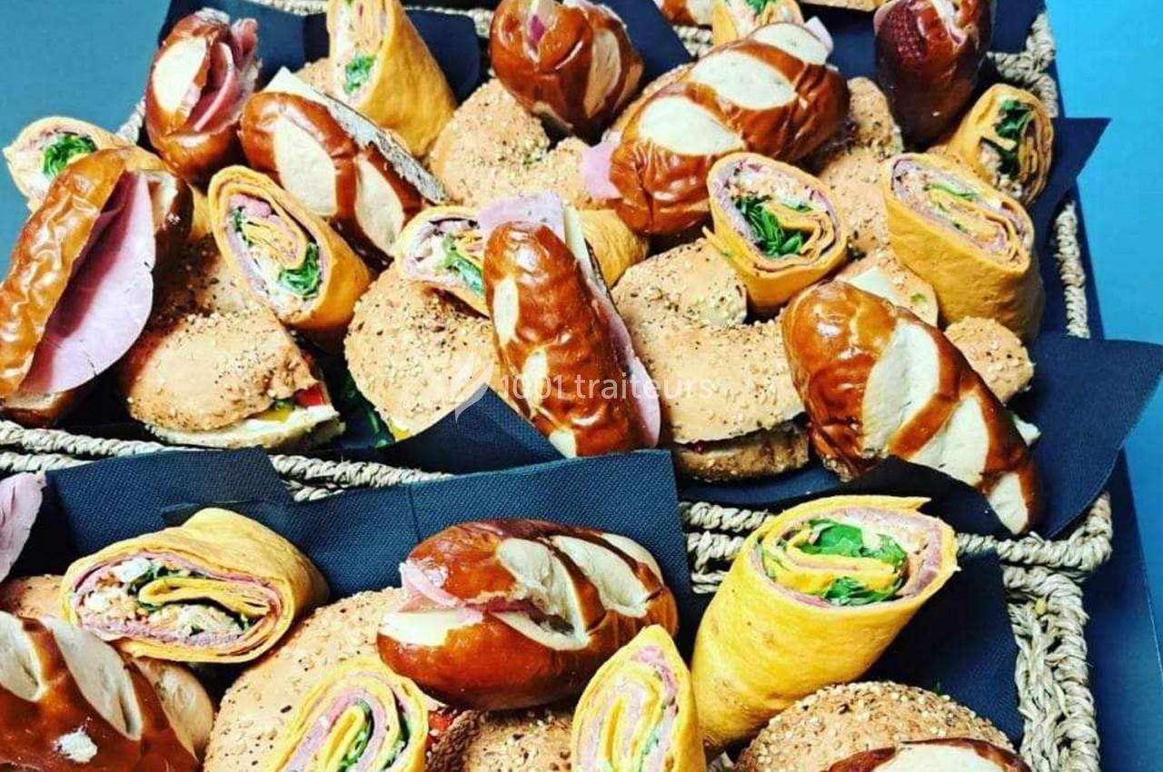 Plateaux garnis de sandwichs variés, incluant des wraps, des pains bretzels et des bagels, sur nappes noires.