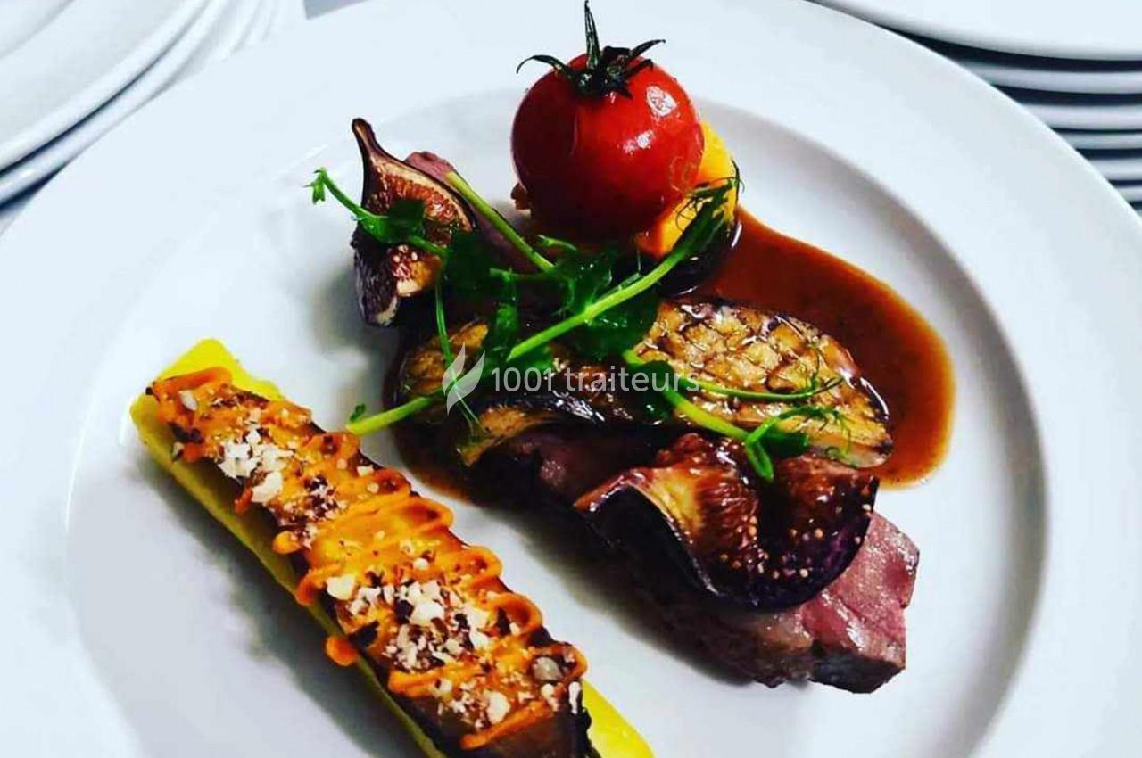 Assiette gastronomique avec viande, figues, tomate rôtie, courgette garnie et sauce, présentée sur une assiette blanche.