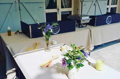 Tables dressées avec nappes beiges, décorées de bouquets de fleurs et d'ustensiles en bois, devant des volets bleus.