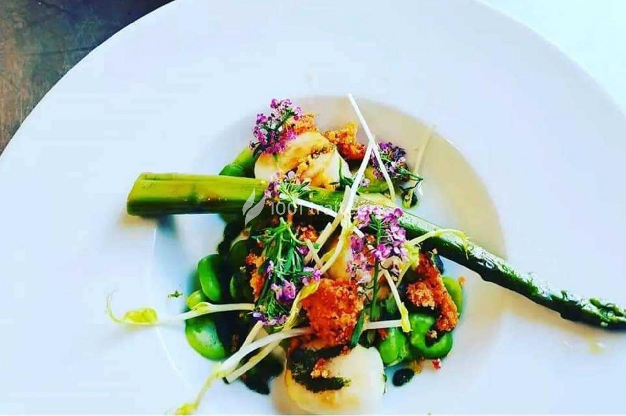 Assiette gastronomique avec asperges, fèves, noix de Saint-Jacques grillées et fleurs comestibles en décoration.