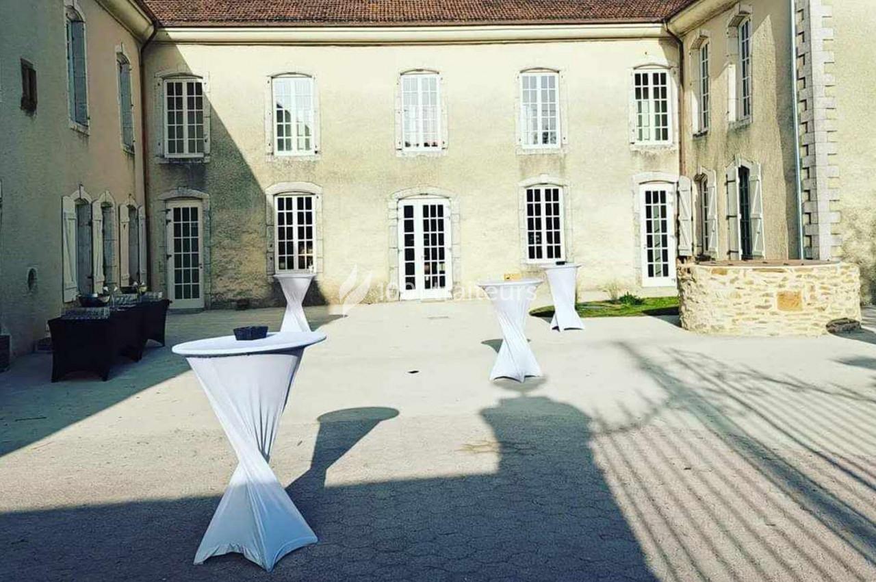 Cour intérieure d'un bâtiment ancien avec tables hautes drapées de blanc, disposées pour un événement en extérieur.