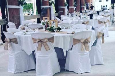 Tables dressées avec nappes beiges, décorées de bouquets de fleurs et d'ustensiles en bois, devant des volets bleus.