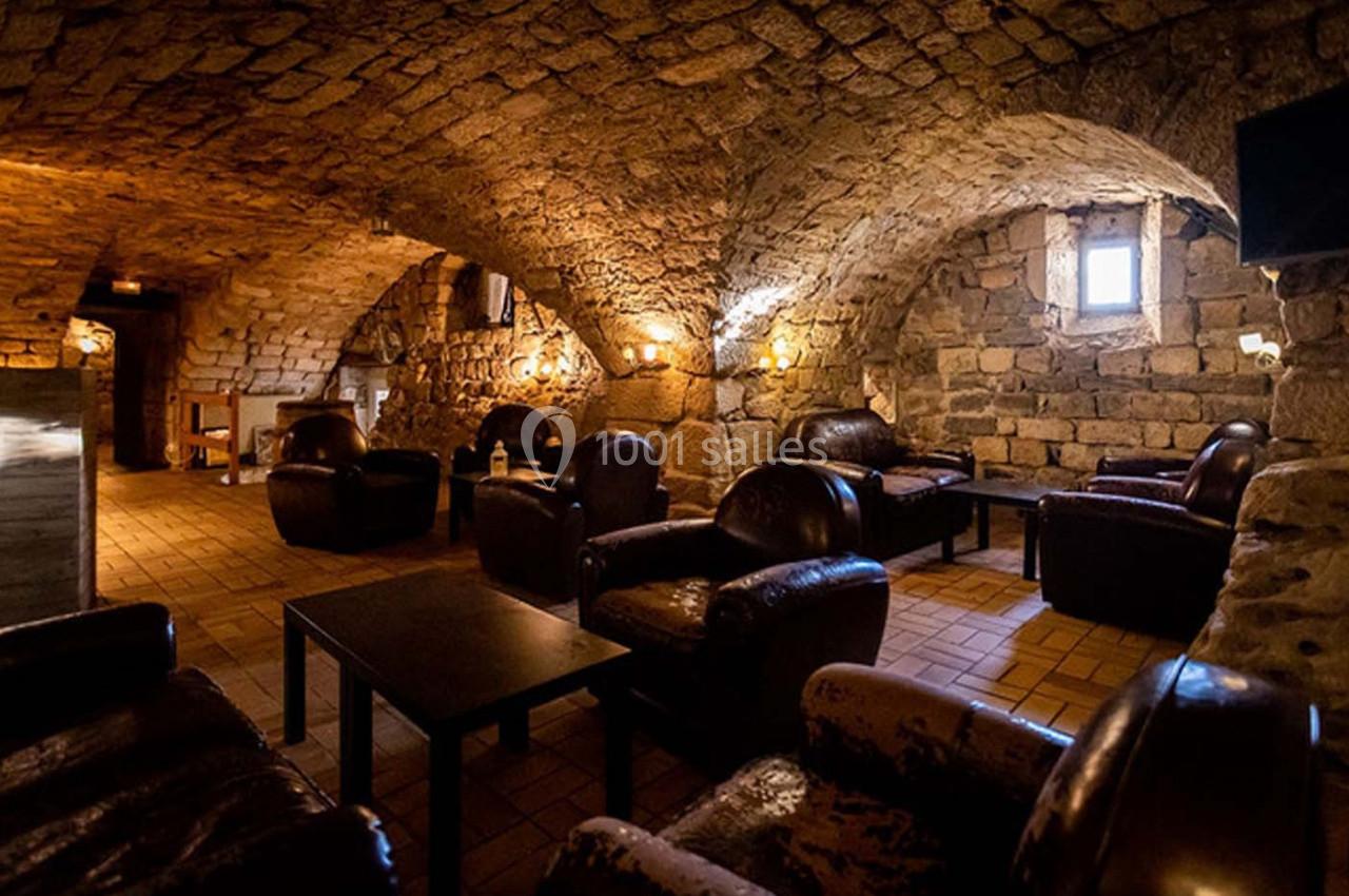 Salon voûté en pierre avec fauteuils en cuir sombre, tables basses et éclairage tamisé.