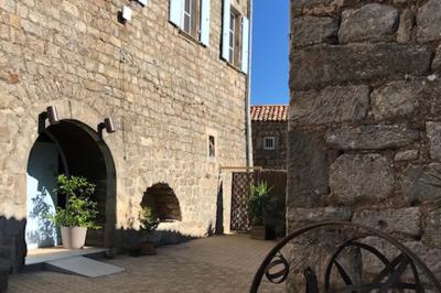Cour pavée entourée de murs en pierre, avec des plantes en pot et une porte voûtée blanche.