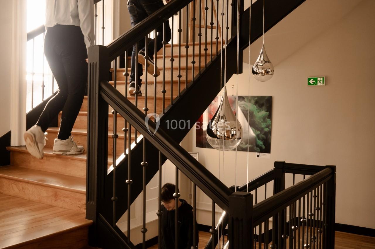 Deux personnes montent un escalier en bois éclairé par la lumière naturelle, une autre descend.