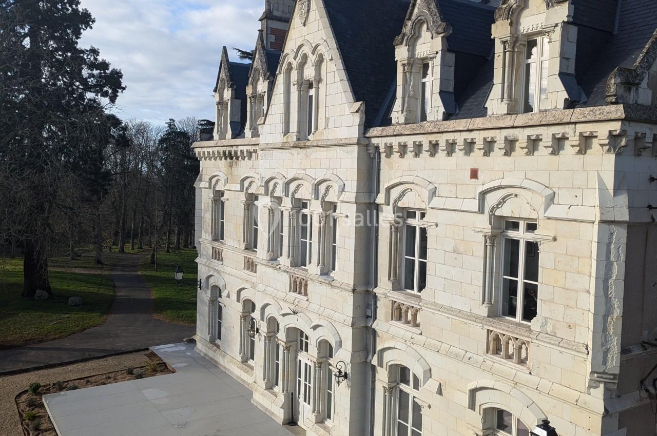 Façade d'un bâtiment historique en pierre blanche avec des toits en ardoise, entouré d'un parc arboré.