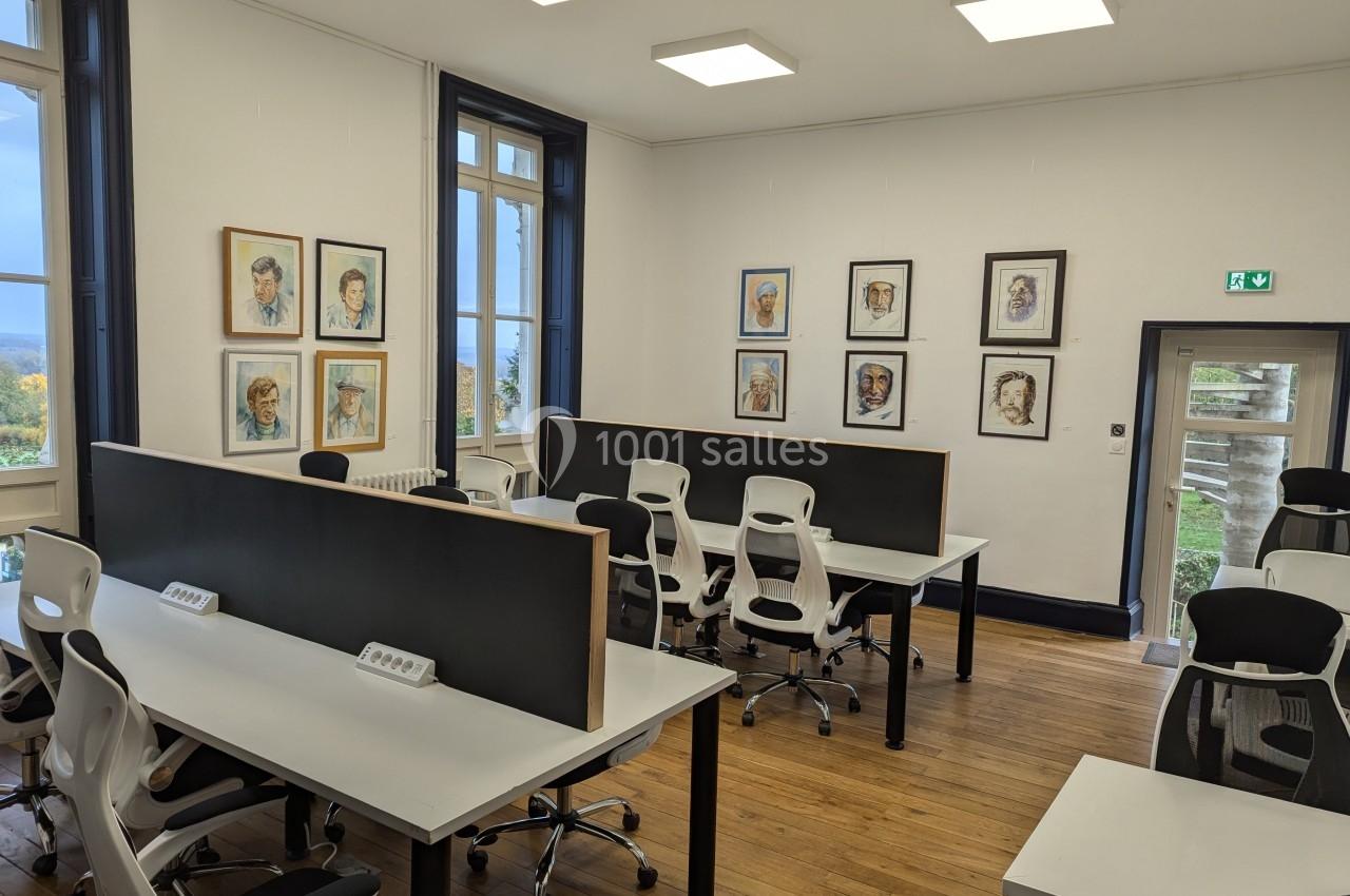 Salle de travail lumineuse avec des bureaux partagés, des chaises ergonomiques et des portraits accrochés aux murs.