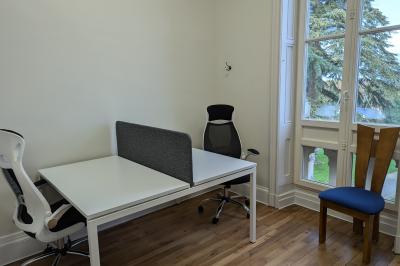 Deux chaises de bureau autour d'une table blanche dans une pièce lumineuse avec parquet et vue sur un jardin.