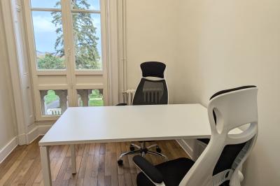 Deux chaises de bureau autour d'une table blanche dans une pièce lumineuse avec parquet et vue sur un jardin.