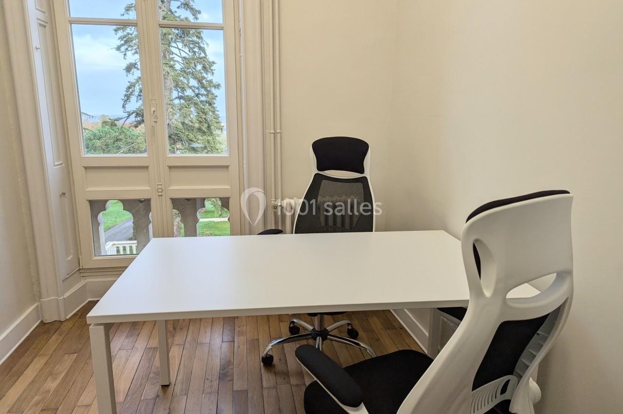 Deux chaises de bureau autour d'une table blanche dans une pièce lumineuse avec parquet et vue sur un jardin.