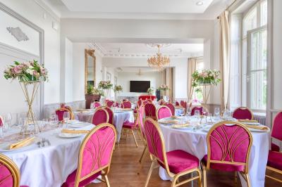 Salle élégante avec tables rondes dressées, chaises rouges et dorées, grand miroir doré et orchidées en décoration.