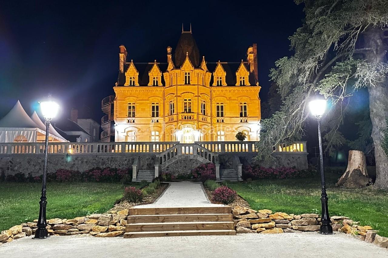 Façade illuminée d'un château de style néogothique la nuit, entourée de lampadaires et d'un jardin aménagé.