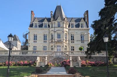 Salle élégante avec tables rondes dressées, chaises rouges et dorées, grand miroir doré et orchidées en décoration.