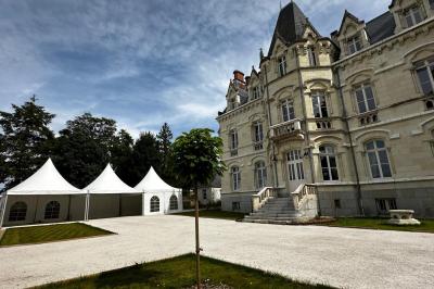 Salle élégante avec tables rondes dressées, chaises rouges et dorées, grand miroir doré et orchidées en décoration.
