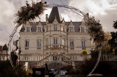 Salle élégante avec tables rondes dressées, chaises rouges et dorées, grand miroir doré et orchidées en décoration.