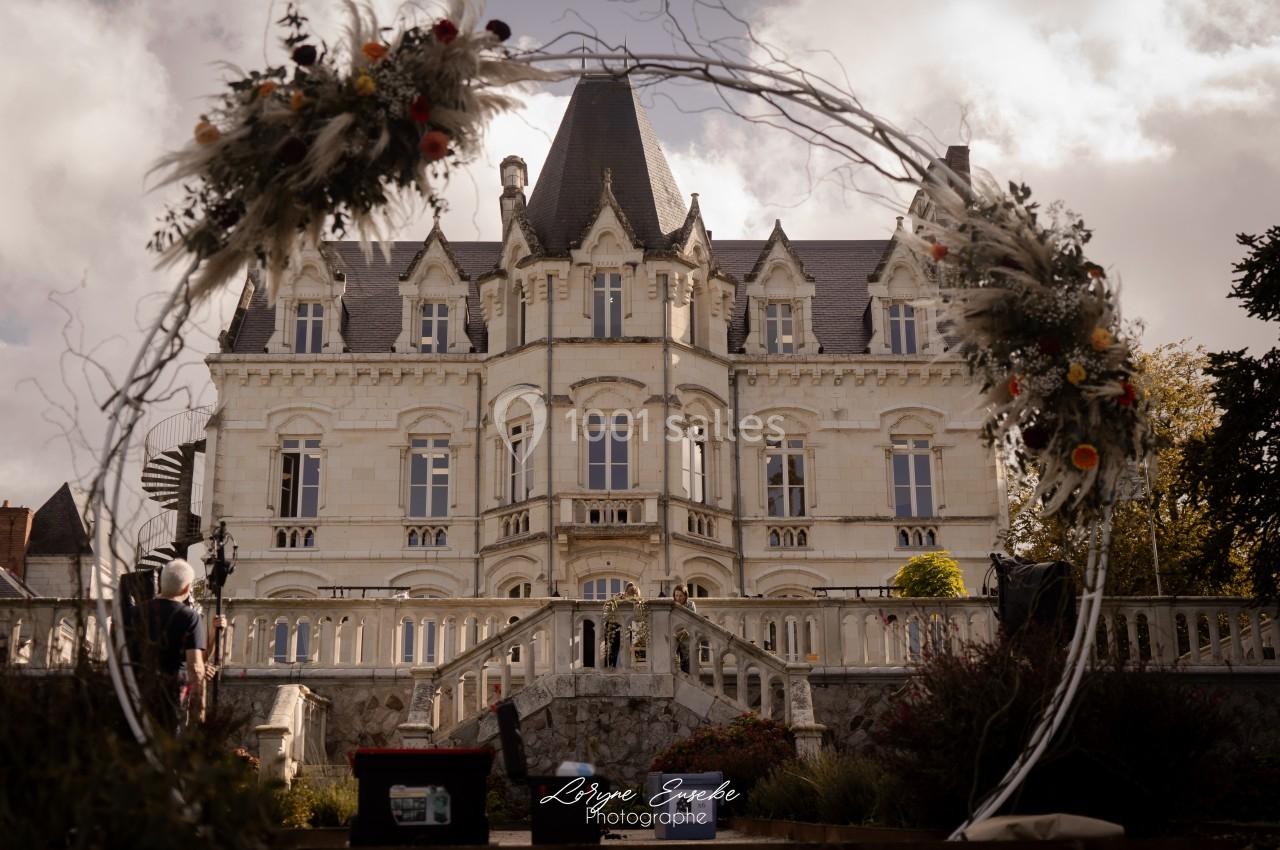Façade d'un château en pierre blanche entouré de végétation, vue à travers un cercle décoratif fleuri.