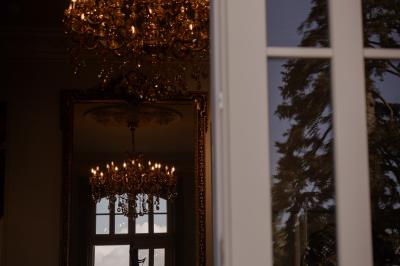Salle élégante avec tables rondes dressées, chaises rouges et dorées, grand miroir doré et orchidées en décoration.