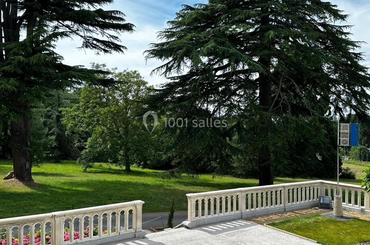 Vue d'un parc verdoyant avec des arbres imposants, prise depuis une terrasse bordée de balustrades blanches.