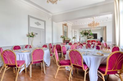 Salle élégante avec tables rondes dressées, chaises rouges et dorées, grand miroir doré et orchidées en décoration.