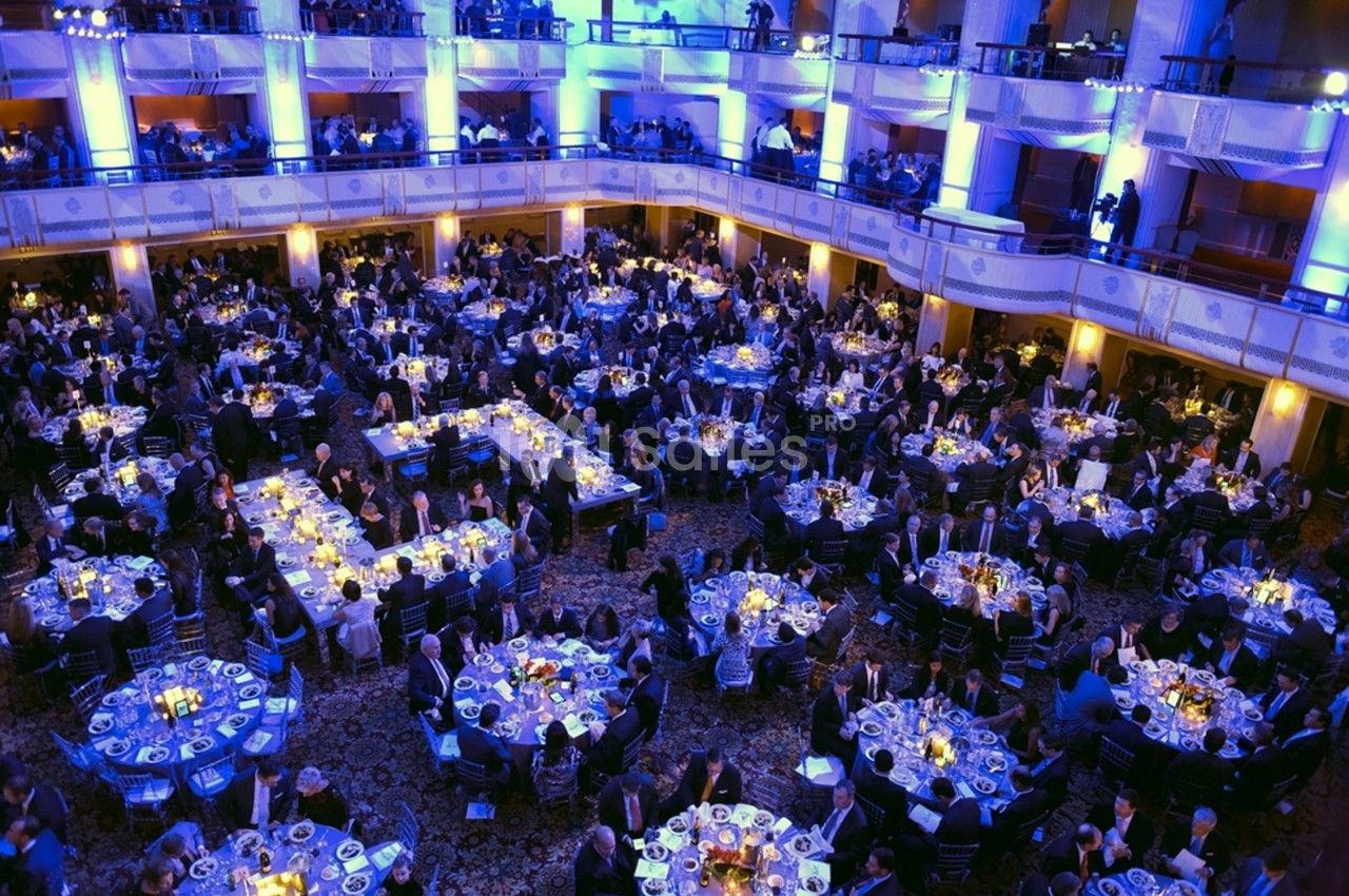 Salle de réception bondée avec des tables rondes dressées, éclairée par des lumières bleues et jaunes.
