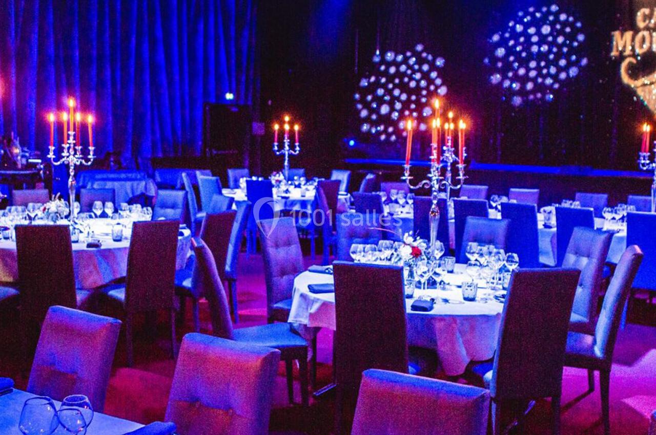 Salle de cabaret avec tables dressées, chandeliers allumés et éclairage tamisé, décorée pour un spectacle.