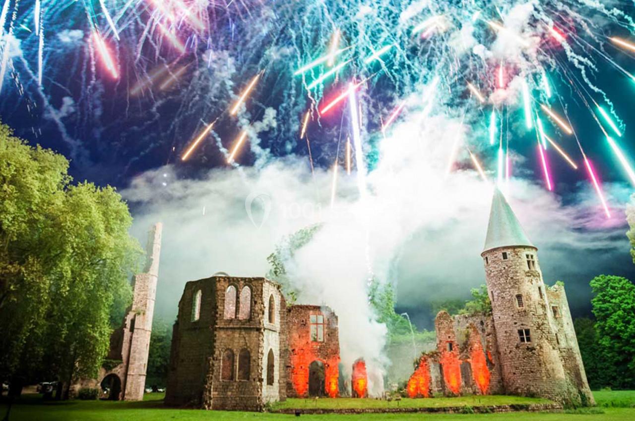 Feu d'artifice coloré illuminant les ruines d'une ancienne abbaye entourée de verdure, de nuit.
