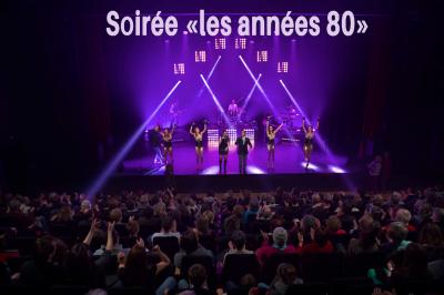 Portraits scintillants de deux figures célèbres réalisés en paillettes sur des panneaux noirs, exposés sur une scène.