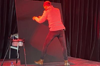 Portraits scintillants de deux figures célèbres réalisés en paillettes sur des panneaux noirs, exposés sur une scène.