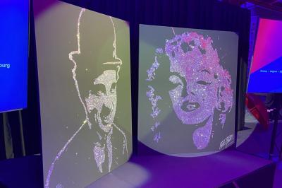 Portraits scintillants de deux figures célèbres réalisés en paillettes sur des panneaux noirs, exposés sur une scène.