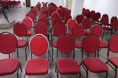 Rangées de chaises rouges alignées dans une salle vide avec un sol en béton et des murs blancs.
