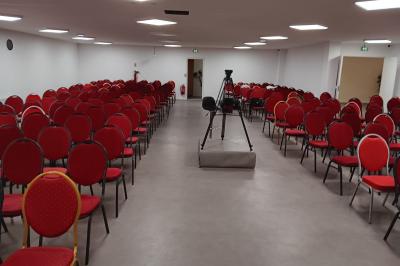 Rangées de chaises rouges alignées dans une salle vide avec un sol en béton et des murs blancs.