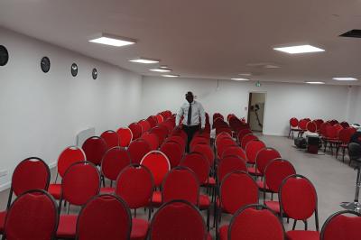 Rangées de chaises rouges alignées dans une salle vide avec un sol en béton et des murs blancs.