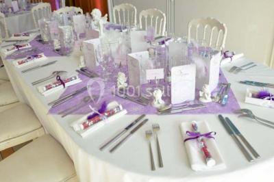 Tente avec table dressée pour un buffet, entourée de chaises blanches, installée sur une pelouse avec haies en arrière-plan.