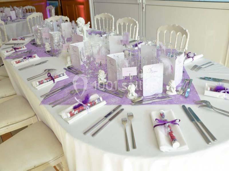 Table dressée avec une nappe blanche, décorations violettes, couverts alignés et menus disposés pour un événement.