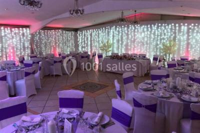 Tente avec table dressée pour un buffet, entourée de chaises blanches, installée sur une pelouse avec haies en arrière-plan.