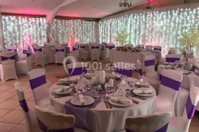 Tente avec table dressée pour un buffet, entourée de chaises blanches, installée sur une pelouse avec haies en arrière-plan.