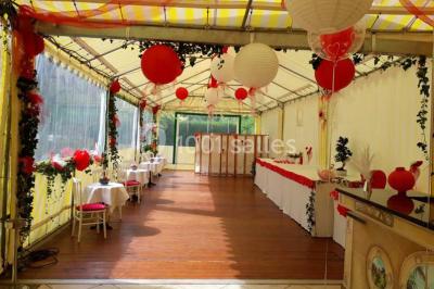 Tente avec table dressée pour un buffet, entourée de chaises blanches, installée sur une pelouse avec haies en arrière-plan.