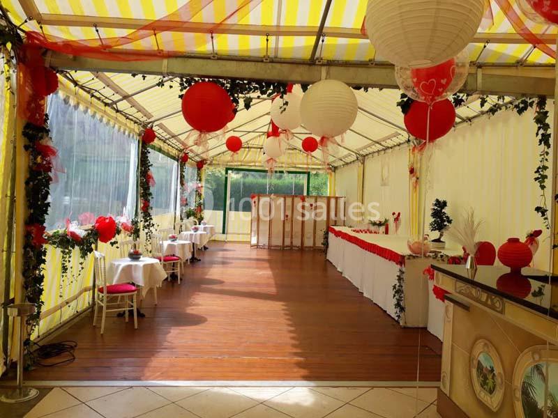 Salle sous tente décorée de lanternes rouges et blanches, tables dressées et ornées pour un événement festif.
