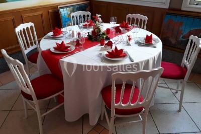 Tente avec table dressée pour un buffet, entourée de chaises blanches, installée sur une pelouse avec haies en arrière-plan.