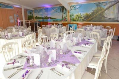 Tente avec table dressée pour un buffet, entourée de chaises blanches, installée sur une pelouse avec haies en arrière-plan.