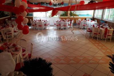 Tente avec table dressée pour un buffet, entourée de chaises blanches, installée sur une pelouse avec haies en arrière-plan.