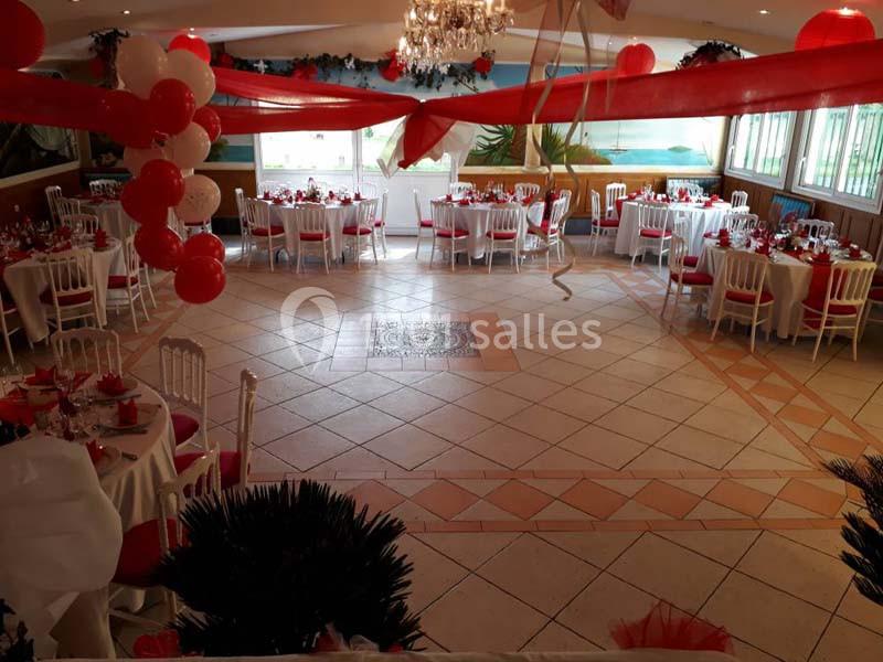Salle de réception décorée avec des ballons rouges et blancs, des nappes assorties et des tables rondes dressées.