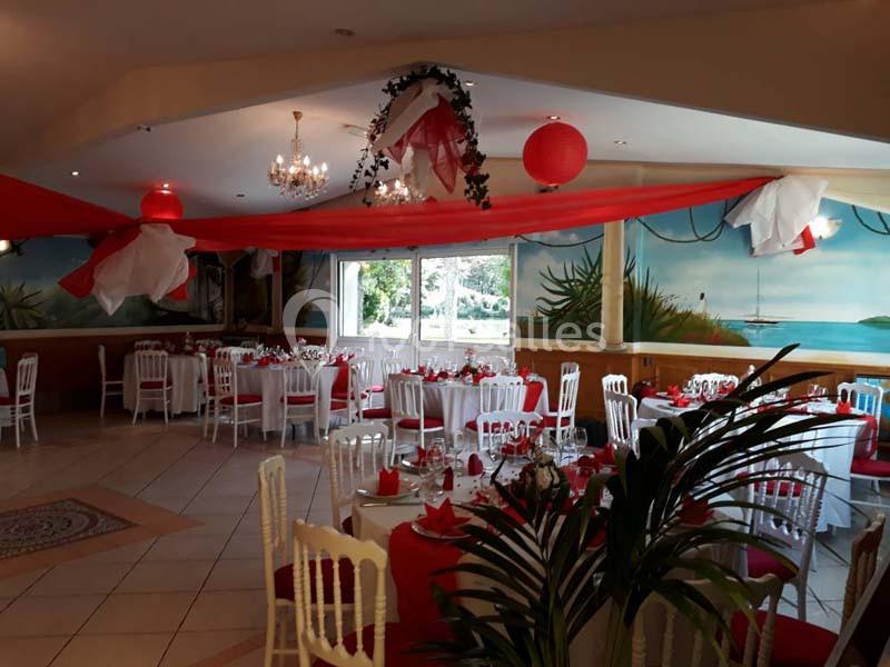 Salle de réception décorée avec des nappes rouges, des chaises blanches et des lanternes suspendues au plafond.