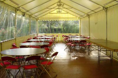 Tente avec table dressée pour un buffet, entourée de chaises blanches, installée sur une pelouse avec haies en arrière-plan.