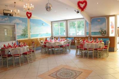 Tente avec table dressée pour un buffet, entourée de chaises blanches, installée sur une pelouse avec haies en arrière-plan.