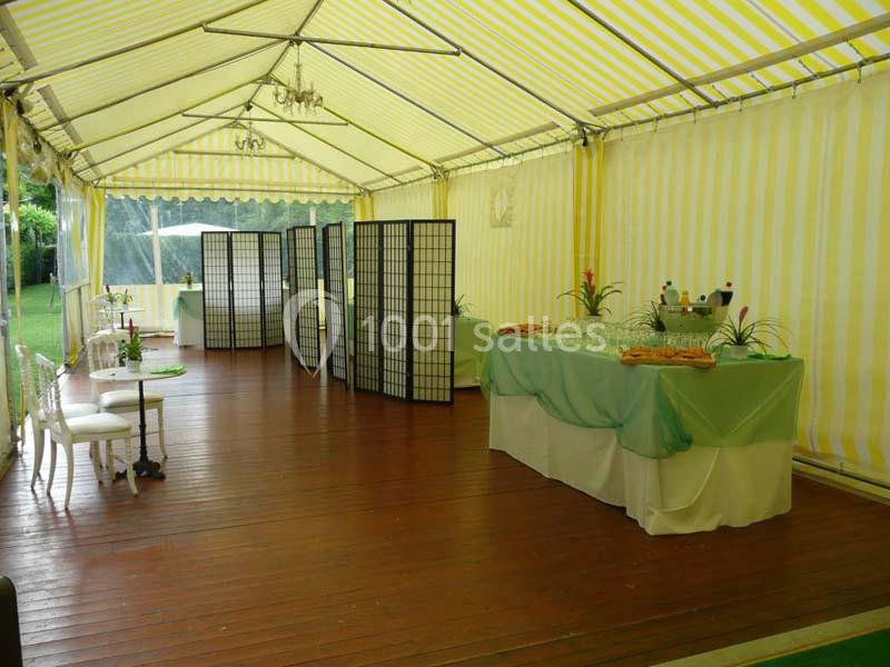 Intérieur d'une tente avec parquet en bois, tables décorées et séparateurs en bois, préparée pour un événement.