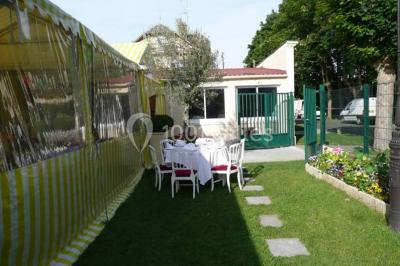 Tente avec table dressée pour un buffet, entourée de chaises blanches, installée sur une pelouse avec haies en arrière-plan.