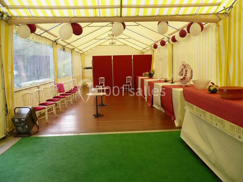 Intérieur d'une tente décorée avec des nappes rouges et blanches, des ballons suspendus et des chaises alignées.
