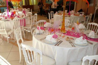 Tente avec table dressée pour un buffet, entourée de chaises blanches, installée sur une pelouse avec haies en arrière-plan.